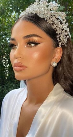 a woman wearing a bridal headpiece in front of some trees and bushes with her eyes closed