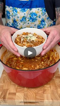 a person in an apron is holding a bowl of chili and cheese over a large red pot