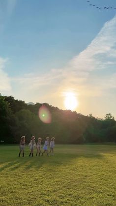 a group of people standing on top of a lush green field under a blue sky