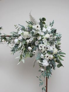 a bouquet of white flowers and greenery on a wooden stand in front of a wall