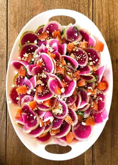 a white plate topped with sliced up radishes and oranges on top of a wooden table