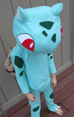 a small child in a blue costume standing on a wooden deck with his feet up