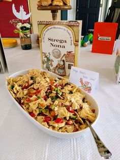 a bowl of pasta with a fork on a table next to a book and card