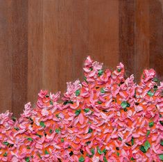 a painting of pink and green flowers on a wooden surface with brown wood in the background