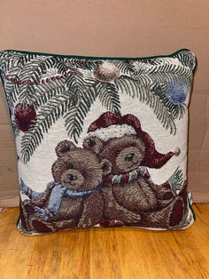 two teddy bears sitting on top of a pillow in front of a wall with christmas decorations