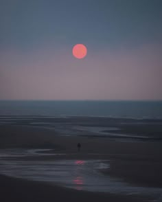 the sun is setting over the ocean and people are walking on the beach at night