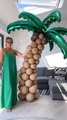 a woman in a green dress standing next to a palm tree made out of balloons