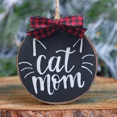 a cat mom ornament hanging on a tree stump with a red and black bow