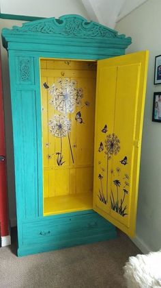 a yellow and blue cabinet with dandelions painted on the doors is in a room