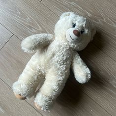 a white teddy bear laying on top of a wooden floor