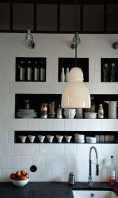 a kitchen with black counter tops and white tile backsplash, hanging light over the sink