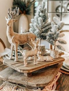 two deer figurines sitting on top of a wooden tray with pine trees in the background