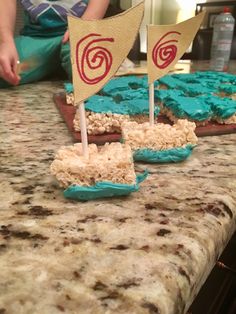 two small sailboats on top of a table with blue frosting and rice krispy kreme