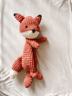 an orange crocheted stuffed animal laying on top of a white bed sheet,