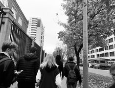 a group of people walking down a sidewalk next to tall buildings on either side of the street