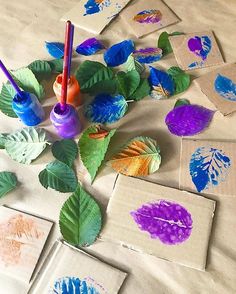 an image of some paper flowers and leaves on a table with paintbrushes in it