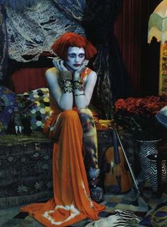 a woman with red hair and makeup sitting on a couch