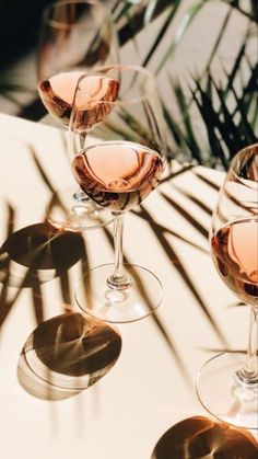 three wine glasses sitting on top of a table next to each other with pink liquid in them