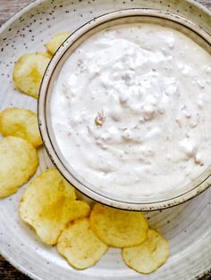 a white bowl filled with dip and chips on top of a wooden table next to a plate