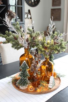 two vases filled with pine cones and evergreen branches on top of a wooden tray