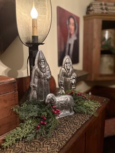 two metal statues sitting on top of a table next to a lamp and pictures in the background