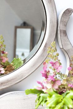 a mirror sitting on top of a table next to a vase with flowers in it