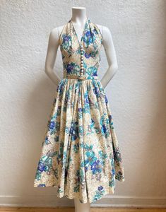 An adorable halter dress perfect for the summer! - 1950's - "Gay Gibson" label - Dress - Shades of blue with white, gray, dark gold, and beige - Cotton - Floral print - Below-the-knee length - Full skirt - Metal zipper at side (does not zip down the entire side, therefore will not go on over broad shoulders) - Eleven white round plastic buttons - One metal snap above buttons - One belt loop - Matching belt - Two hanger straps - *Petticoat underneath not included  *Mannequin's Measurements: Bust: 33", Ribcage: 28 1/2", Waist: 24 ½", Hips: 34 ½"  Measurements: - Bust: up to 34"  - Ribcage (below bust): 29" (was snug on our mannequin) - Waist: 25" - Hips: Free - Side seam under arm to waist: 9 1/2" - Waist to hem: 28 1/2" - Nape of neck to back of waist: 19"  - Nape of neck around to front of Retro Sleeveless Halter Dress For Summer, Fitted Retro Sleeveless Halter Dress, 1950s Blue Summer Dress, 1950s Style Blue Vintage Dress For Summer, 1950s Style Blue Summer Dress, Summer Sleeveless Vintage 1950s Style Dress, Blue 1950s Style Vintage Summer Dress, 1950s Style Sleeveless Summer Vintage Dress, Blue 1950s Style Summer Dress