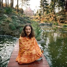 a man sitting on top of a wooden dock next to a lake covered in an orange blanket