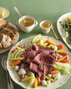 a table topped with plates of food next to bread and salad on top of it