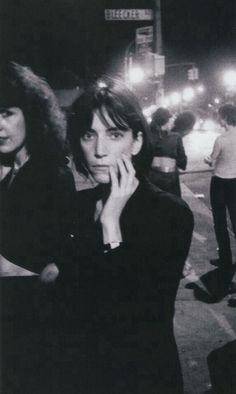 black and white photograph of two women standing on the street at night with people in the background