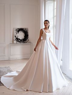 a woman in a white wedding dress standing next to a window with her hands on her hips