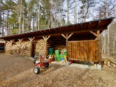 a small wooden building with logs stacked on the side and a lawn mower parked in front