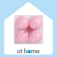 four pink christmas ornaments in a clear plastic box with the at home logo on it