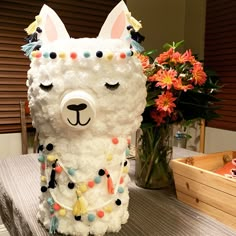 a white llama cake sitting on top of a table next to a vase filled with flowers