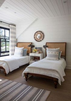 two beds in a bedroom with white walls and wood flooring, along with striped rugs