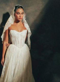 a woman in a wedding dress with a veil on her head and hands behind her back