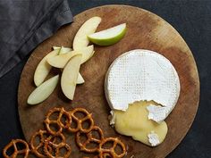 an apple, cheese and pretzels on a wooden plate