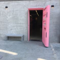 an open door with a bench in front of it on the concrete floor next to a wall