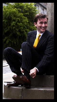 a man in a suit and tie sitting on the steps with his feet crossed, smiling