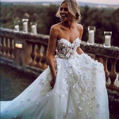 a woman in a white wedding dress standing on a balcony next to candles and flowers