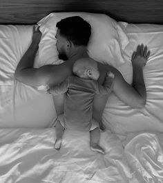 a man laying in bed next to a baby on top of it's back