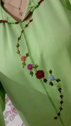 a woman wearing a green top with flowers on it's neck and beads hanging down the side