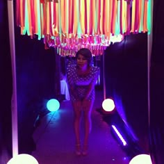 a woman standing in the middle of a room with colorful lights hanging from it's ceiling