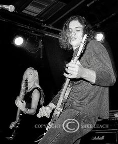 a man holding a guitar while standing next to a woman on the other side of a stage