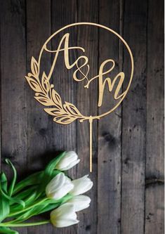 a wedding cake topper with the initials on it and flowers in front of a wooden background