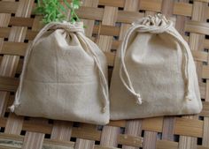 two linen bags sitting on top of a wooden table next to a green plant in a vase