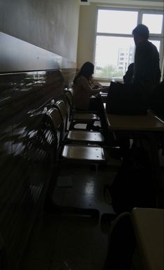 two people sitting at desks in a room with large windows and no one on the bench