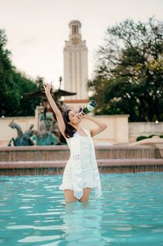 a woman in a white dress is standing in the water and drinking from a bottle