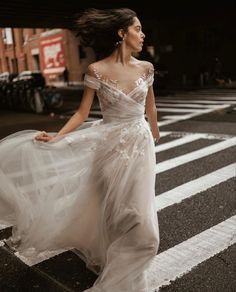 a woman in a white dress is crossing the street with her hair blowing in the wind