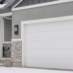 a white garage door in front of a gray house with snow on the ground and trees